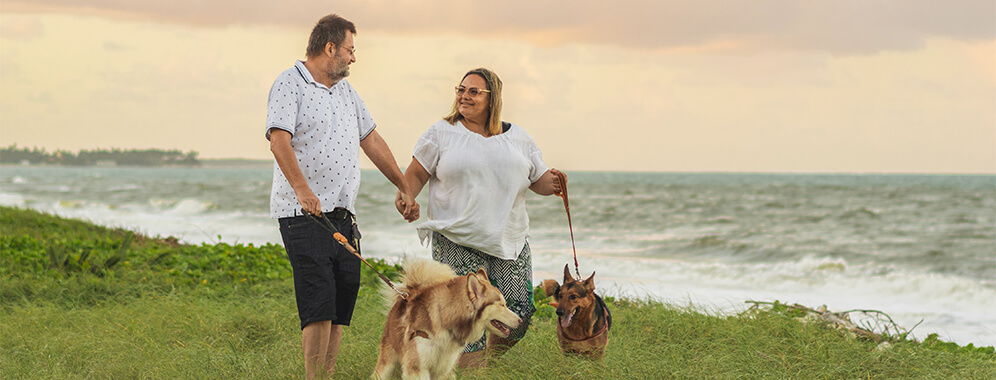 Ein Paar geht am Meer mit zwei Hunden spazieren.