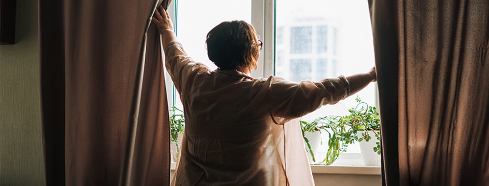 Eine Frau öffnet die Vorhänge am Fenster.