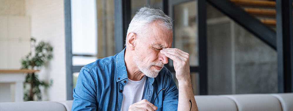 Ein Mann schließt die Augen und hält sich die Nasenwurzel. 