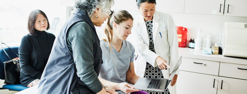 Mehrere Personen sitzen in einer Praxis um einen Laptop herum und besprechen etwas. 