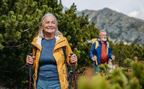 Eine Frau und ein Mann sind aktiv mit Walkingstöcken in den Bergen unterwegs. 