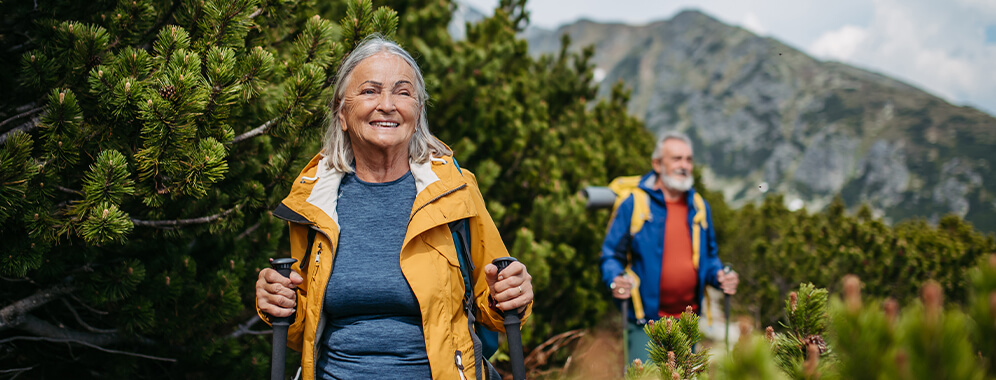Eine Frau und ein Mann sind aktiv mit Walkingstöcken in den Bergen unterwegs.