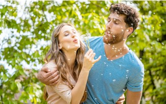 Paar bläst Pusteblumen. Mann mit Bart, Frau mit langen Haaren.