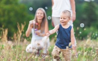 Familie spielt mit Seifenblasen. Kind im Vordergrund, Eltern im Hintergrund.