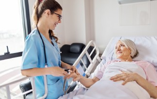 Ärztin untersucht Patientin im Bett. Patientin lächelt.