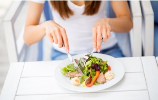Person isst Salat mit Messer und Gabel auf einem Tisch im Freien.