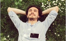 Mann liegt im Gras. Mann mit Kopfhörern und Smartphone. Sonniger Tag.