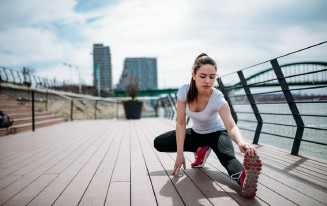 Frau dehnt sich draußen. Sportkleidung. Stadt im Hintergrund.