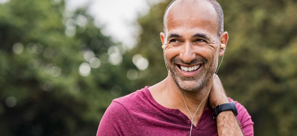 Ein Mann mit einem Lächeln, der Kopfhörer trägt und sich im Freien befindet.