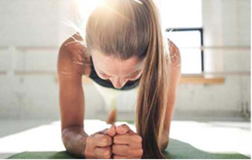 Eine Frau macht Plank-Übung auf einer Matte. Sie trägt Sportkleidung und hat lange Haare.