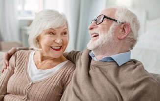 Älteres Ehepaar lacht. Frau stützt sich auf Mann.