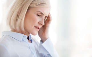 Frau mit Kopfschmerzen, Hand an der Schläfe. Bluse. Nahaufnahme. Hintergrund unscharf.