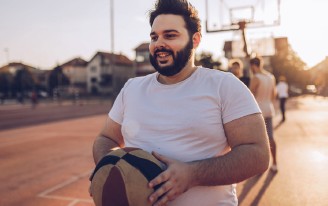Ein Mann mit Bart hält einen Ball auf einem Basketballplatz. Er lächelt.
