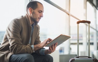 Mann sitzt mit Tablet und Koffer. Wartet am Flughafen.