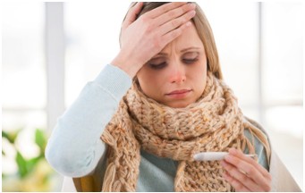 Frau mit Schal und Fieberthermometer. Sieht krank aus.