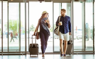 Ein Paar mit Gepäck in einer Flughalle. Beide tragen Koffer und lächeln.