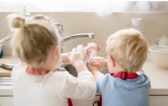 Zwei Kinder waschen sich die Hände in einer Küche. Sie tragen Schürzen.