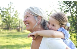 Ältere Frau und junges Mädchen umarmen sich. Das Mädchen sitzt auf dem Rücken der Frau.