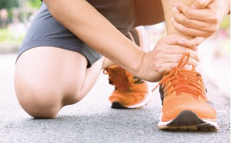 Person liegt auf dem Rücken, Bein angewinkelt, Yoga-Matte, schwarze Kleidung.