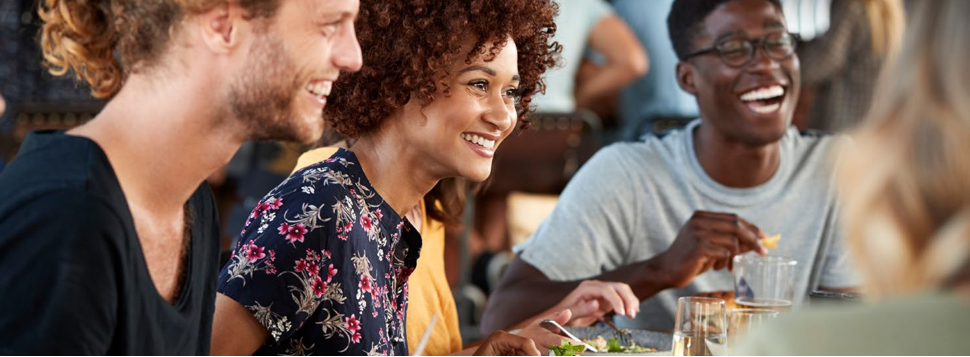 Menschen sitzen an einem Tisch und lachen. Sie unterhalten sich und essen zusammen.