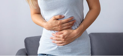 Frau hält sich den Bauch. Sie scheint Schmerzen zu haben.