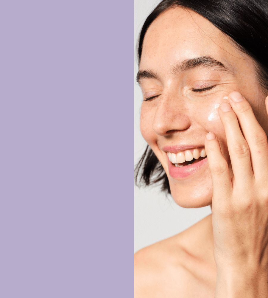 Frau mit Serum auf Gesicht. Lila Hintergrund. Hautpflege. Lächelnd.