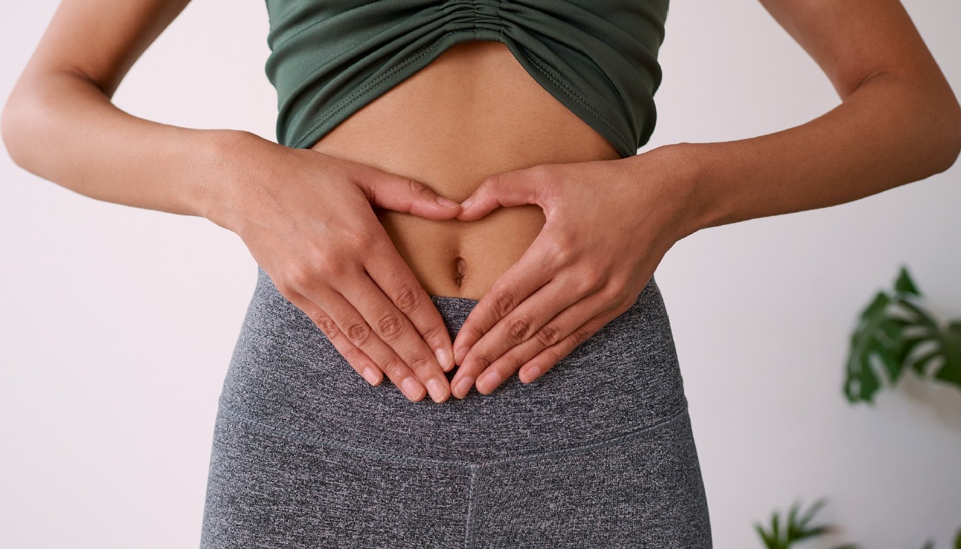 Nahaufnahme einer Person, die mit den Händen ein Herz über dem Bauch formt. Sportkleidung.