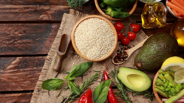 Draufsicht auf eine Auswahl an Lebensmitteln: Gemüse, Kräuter, Öl, Avocado, Tomaten, Gewürze.