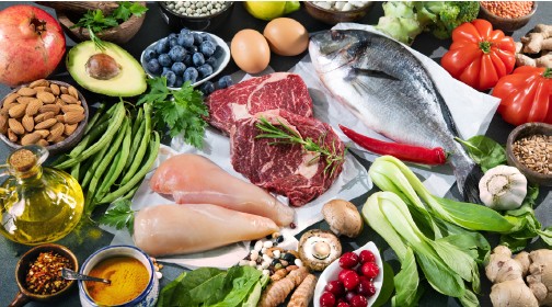 Verschiedene Lebensmittel auf einer Oberfläche. Enthalten Fleisch, Fisch, Gemüse, Obst und Nüsse.