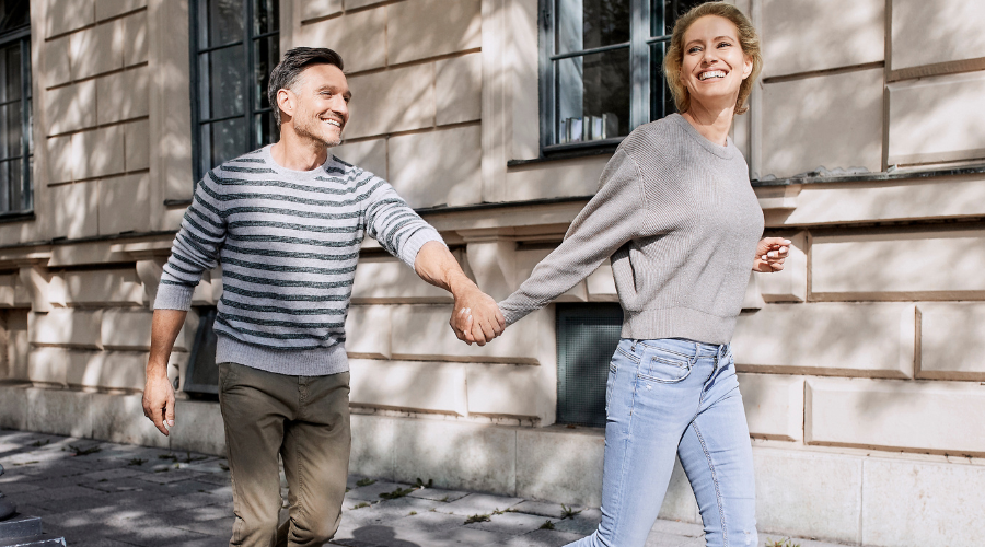 Paar geht Hand in Hand. Mann und Frau, helle Kleidung, sonniges Licht.