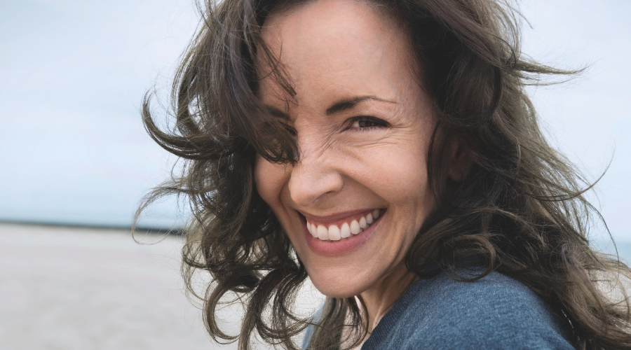 Lächelnde Frau mit langen Haaren. Strand im Hintergrund.