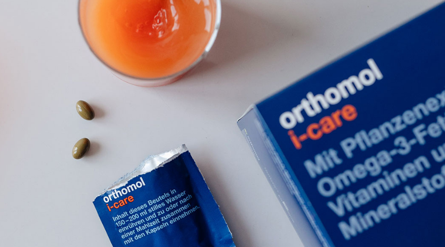 Produktverpackung, Beutel und Kapseln. orthomol i-care Beutel. Glas mit Flüssigkeit.