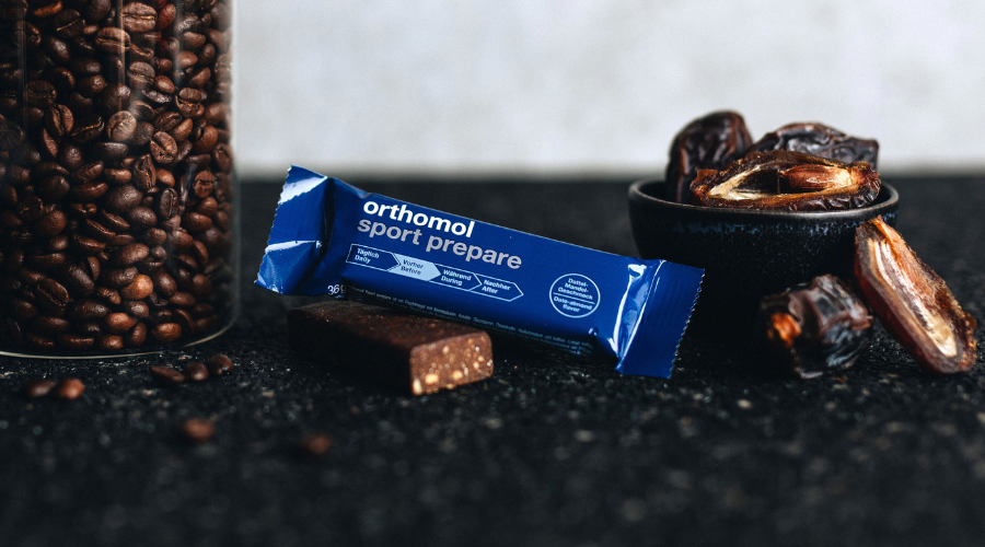 Riegel, Kaffeebohnen und Datteln. Text: Orthomol sport prepare. Schoko-Mandel-Dattel.