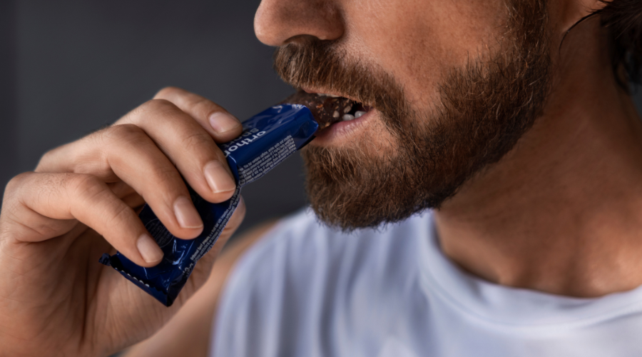 Mann isst einen Riegel. Text: Orthomol sport prepare. Schoko-Mandel-Dattel-Geschmack.