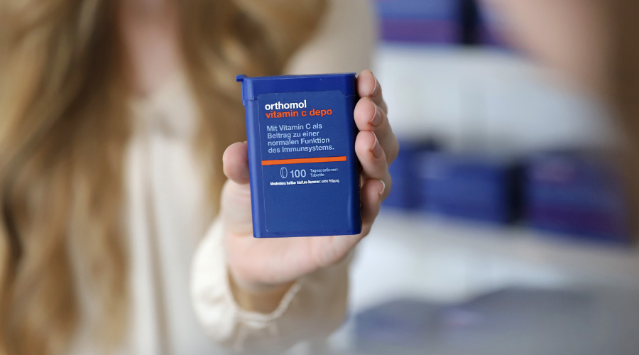 Person hält blaue Tabletten-Behältnis. Orthomol Vitamin C depo. Text: Für Immunsystem.