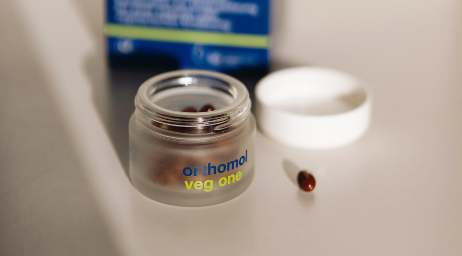 Dose mit Kapseln. Kapseln in einem transparenten Behälter. Produktname Orthomol veg one.