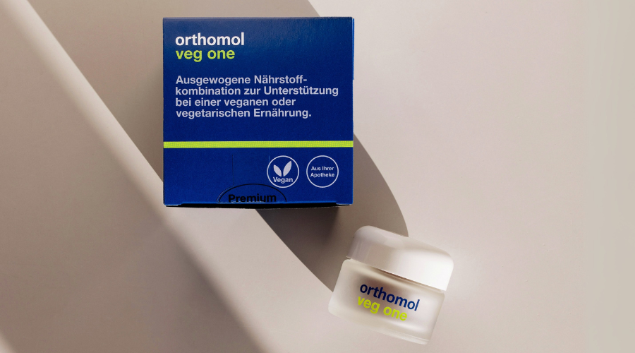Orthomol veg one-Packung und Dose. Blaue Schachtel und Dose mit Kapseln. Produktname sichtbar.