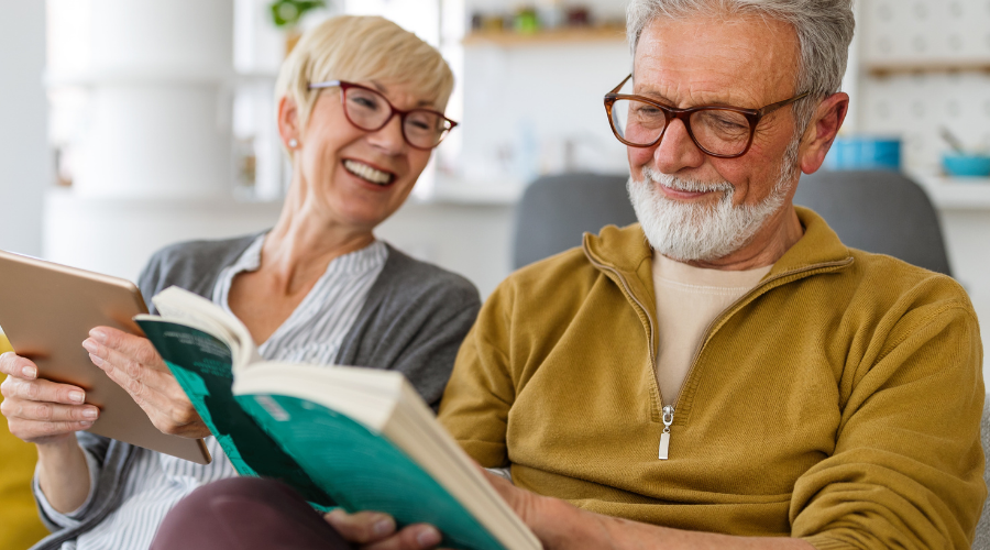 Älteres Ehepaar liest. Mann mit Brille, Buch. Frau mit Tablet.