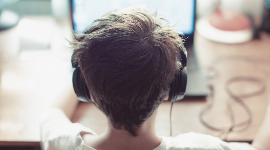 Junge mit Kopfhörern vor Laptop. Konzentriert. Hintergrund: Schreibtisch mit Kabeln.